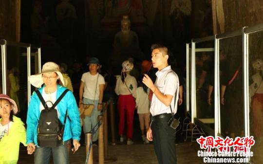 2018年，敦煌莫高窟经历着近40年来同期最大的客流冲击，为寻求文物安全和提供服务的“中间点”，敦煌研究院通过3个月的课堂培训和实地培训，选拔优秀大学生成为志愿讲解员，为游客讲解莫高窟。图为志愿讲解员为游客讲解洞窟。　高军德 摄